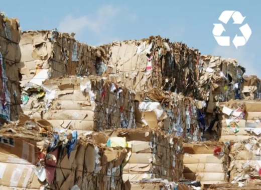 Samengeperste balen oud karton en papier op een recyclingterrein met recycle-symbool